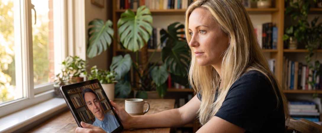 Mulher em sessão de psicoterapia on-line por tablet, em casa, com plantas e luz natural da janela